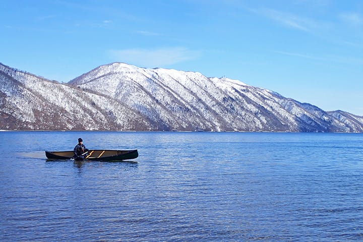 早春の残雪風景の支笏湖にてカナディアンカヌーを漕ぐ