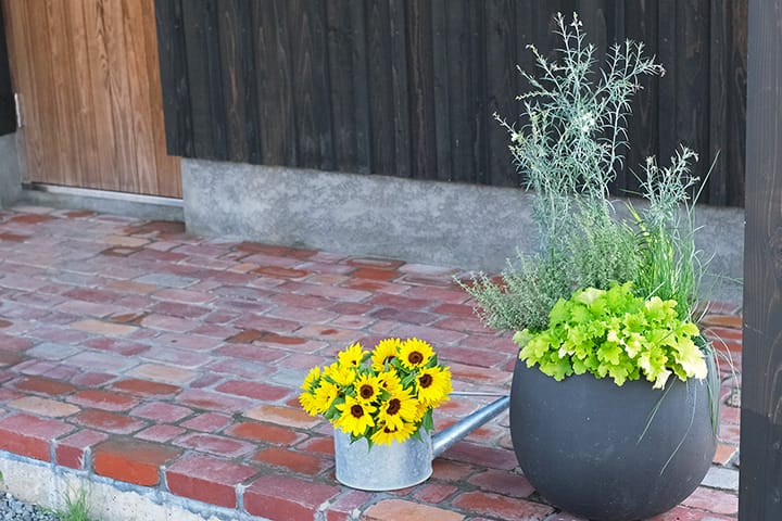 レンガ敷きの玄関ポーチと鉢の緑とひまわり