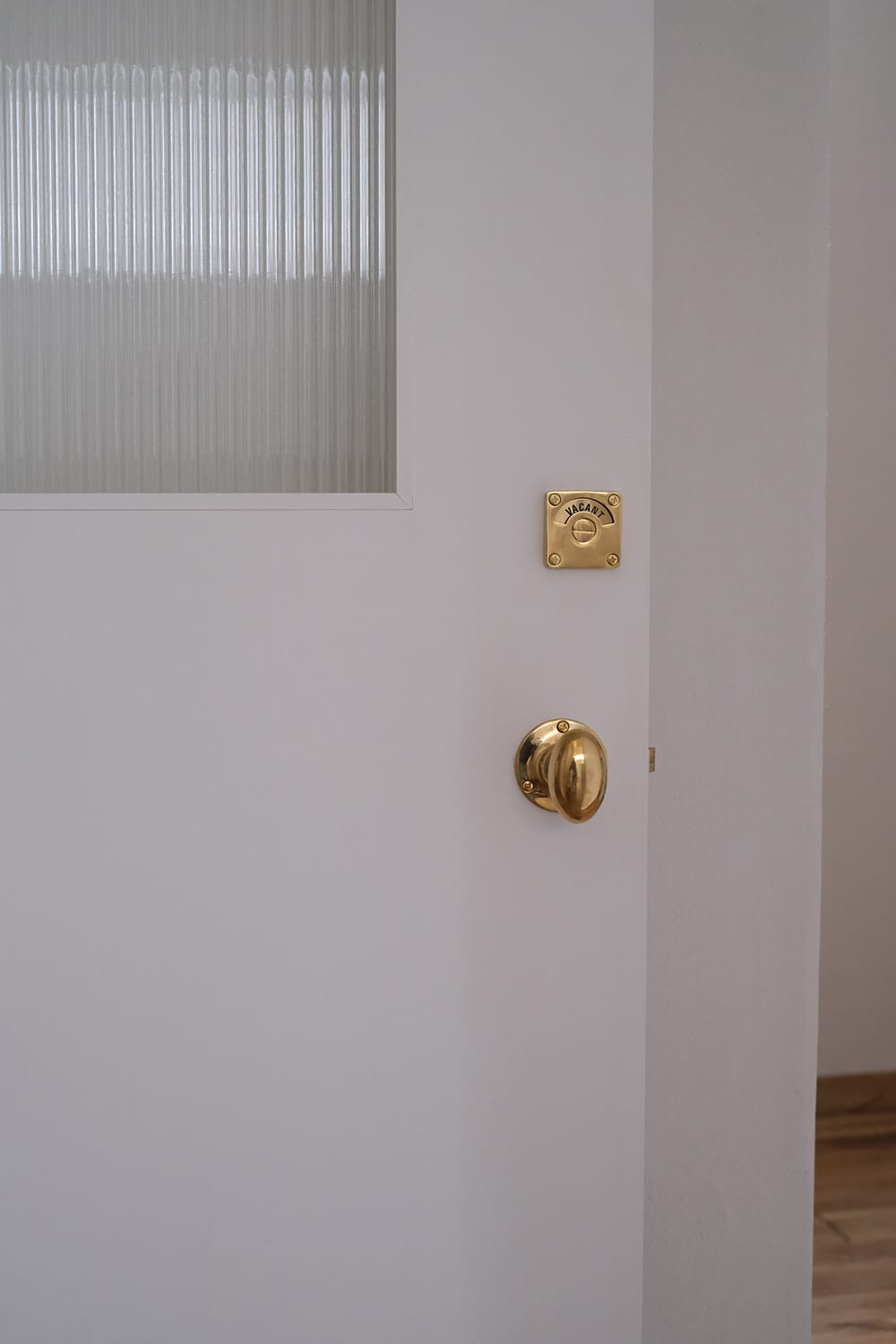 真鍮ドアノブと表示錠と縦縞モールガラスの白いドアは白い塗り壁と同化する