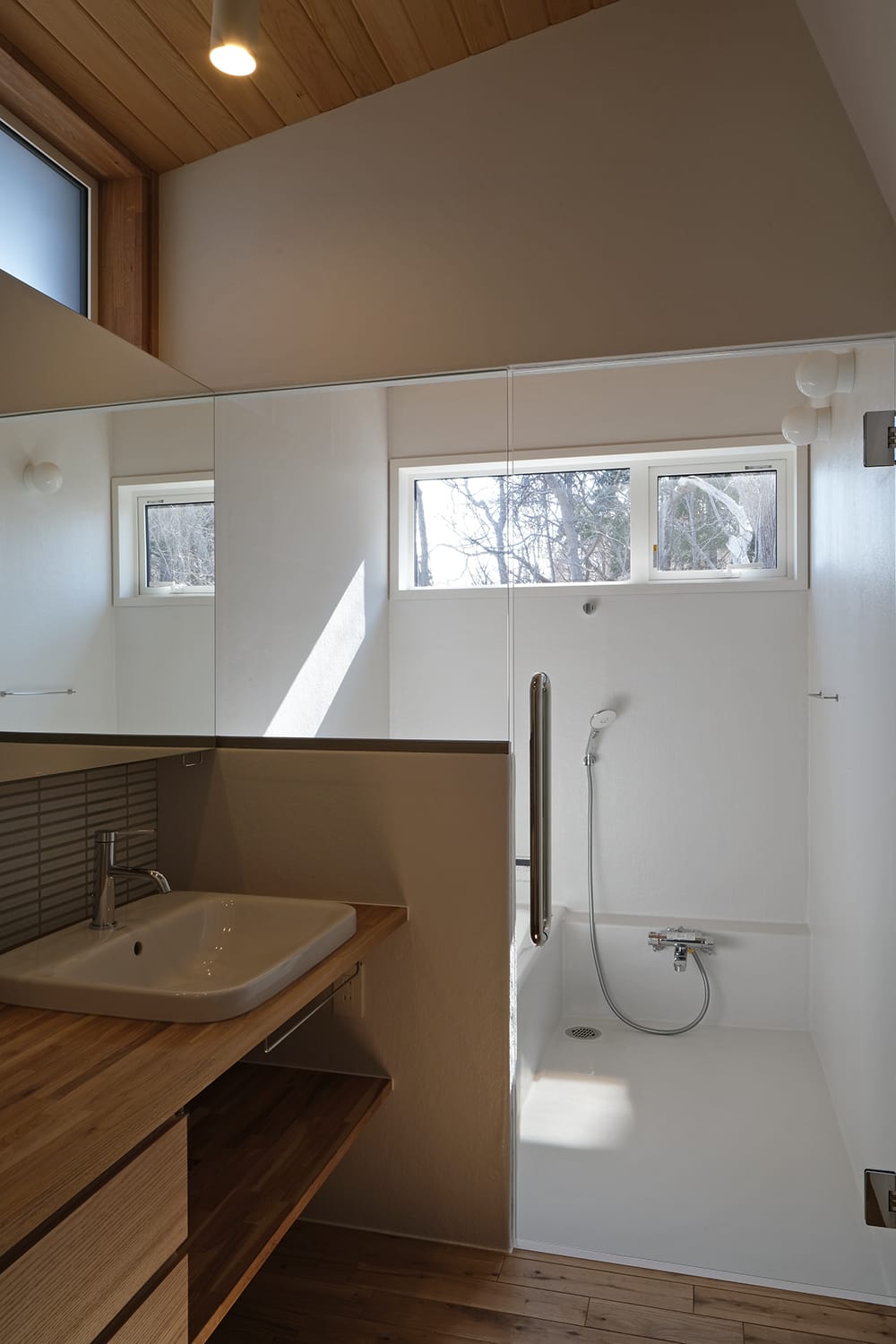ガラスドアとガラスパーテーションで透けて繋がる明るいバスルームと洗面脱衣室