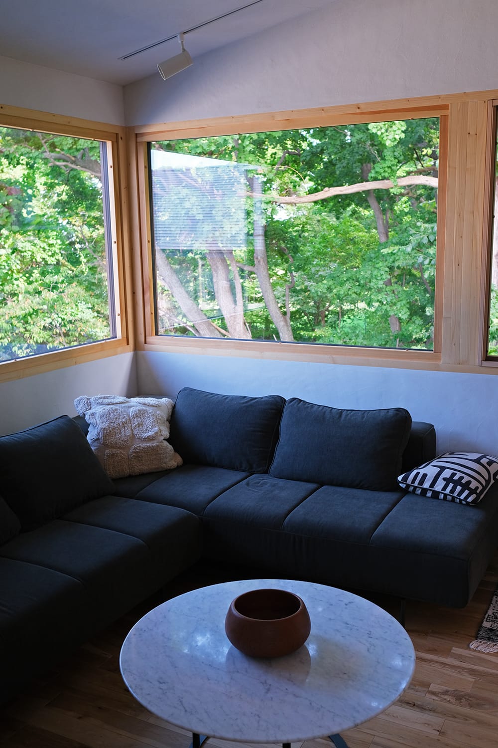 コーナー木枠窓から見える原生林の緑とL型ソファー