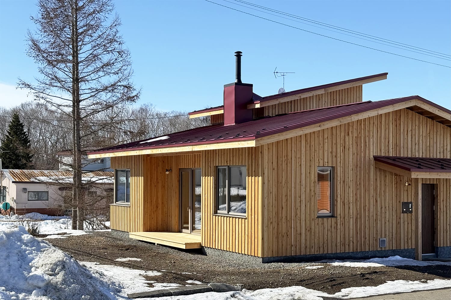 北海道産カラマツ無垢板張りの外壁の家 あずき色の屋根 薪ストーブのある家