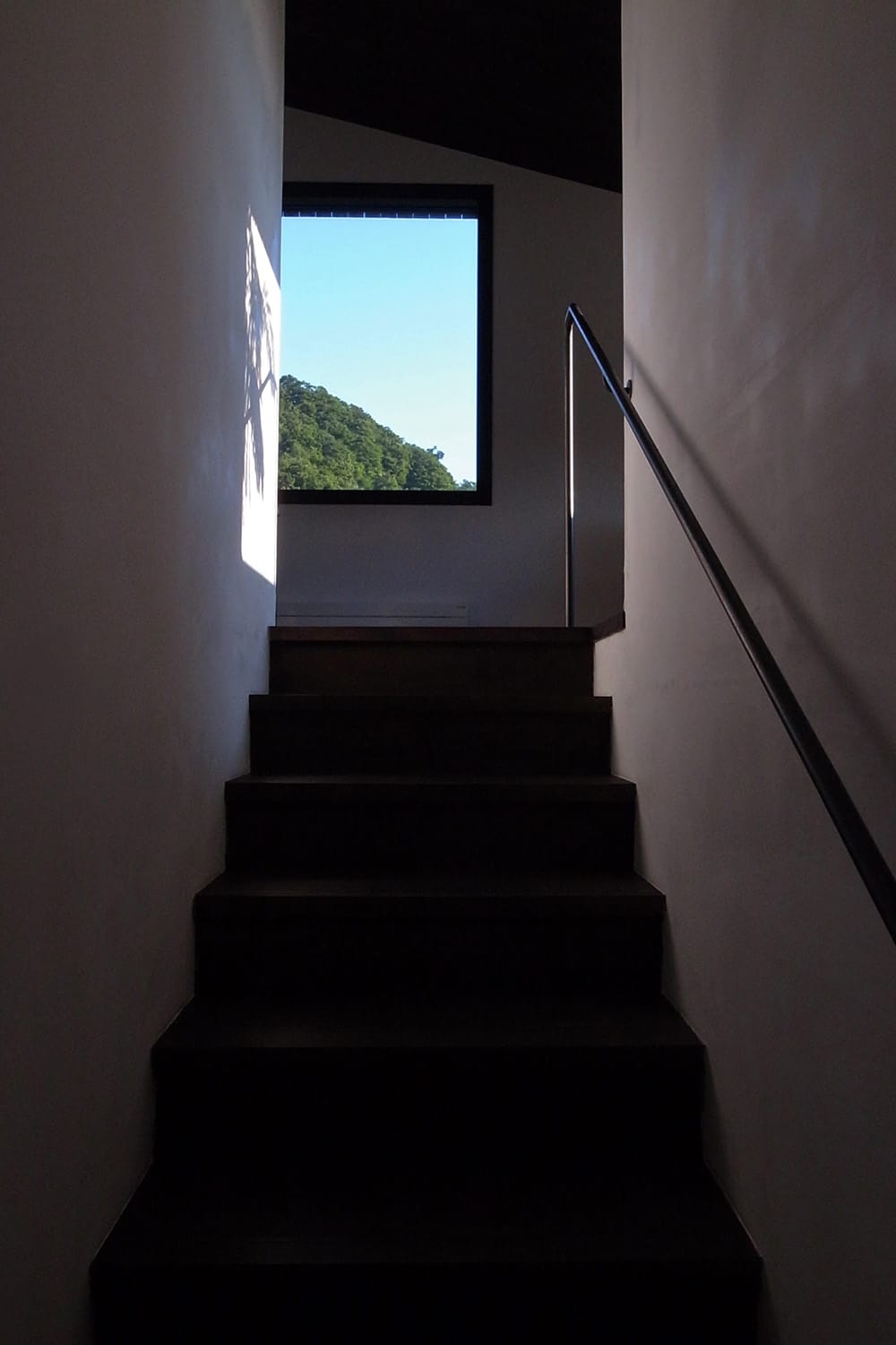 真っ直ぐな階段をのぼった先に見える窓と山の緑と空の青