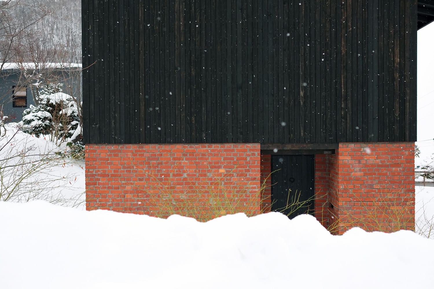 雪が積もる中に建つ赤レンガ積みと墨色の板張りの家