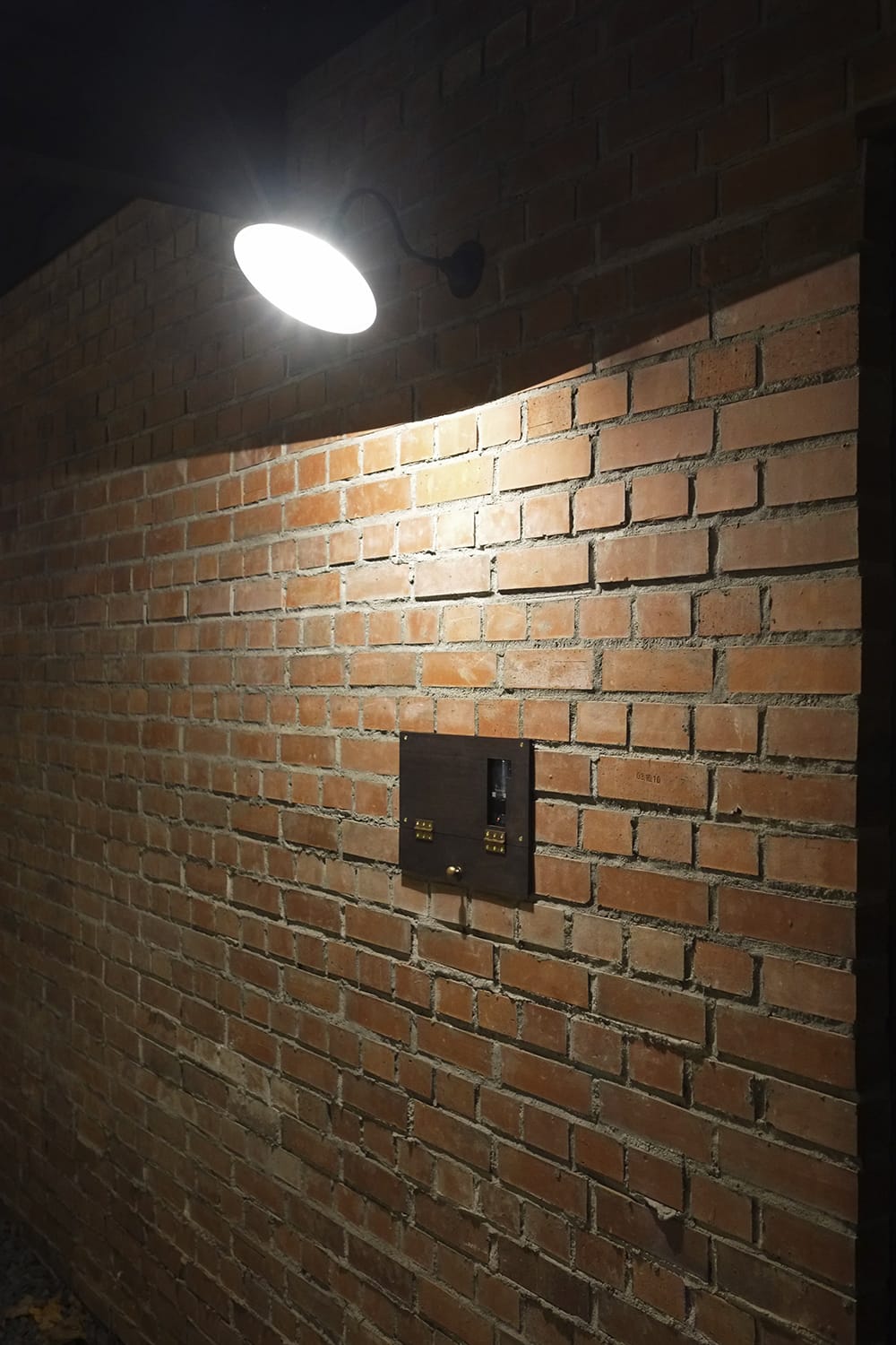 赤煉瓦積みの壁とポーチライトと木製プレートに明かりが灯る