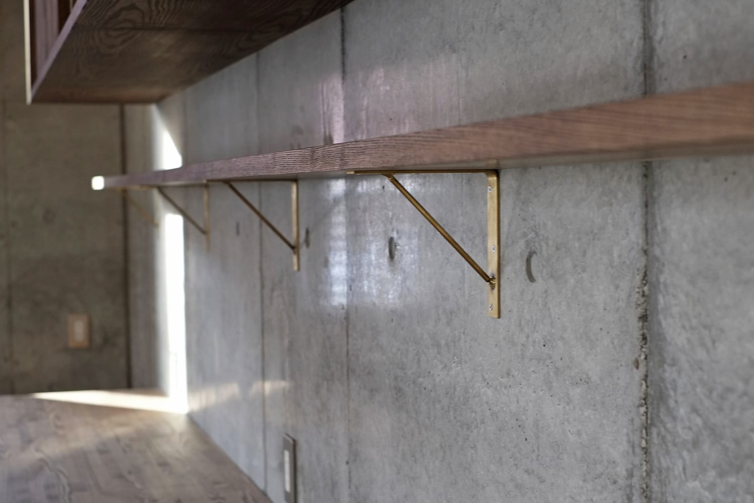 コンクリート打ち放しの壁にタモの棚板と真鍮のブラケット