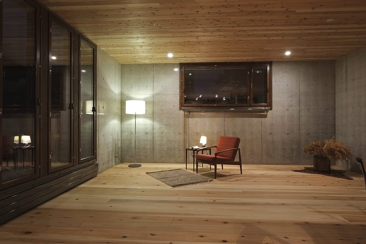杉板張りの床と天井とコンクリート打放しの壁の室内に明かりが灯る1