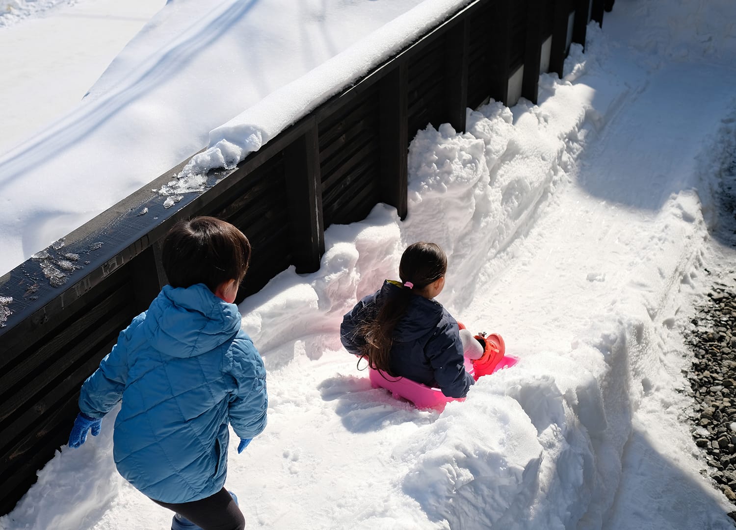 中庭につくった雪山でソリ滑りして遊ぶ子供たち