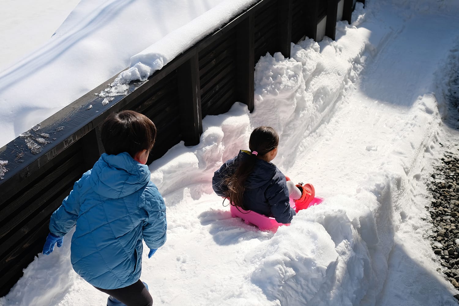 中庭に作った雪山からソリで滑り降りて遊ぶ子供たち