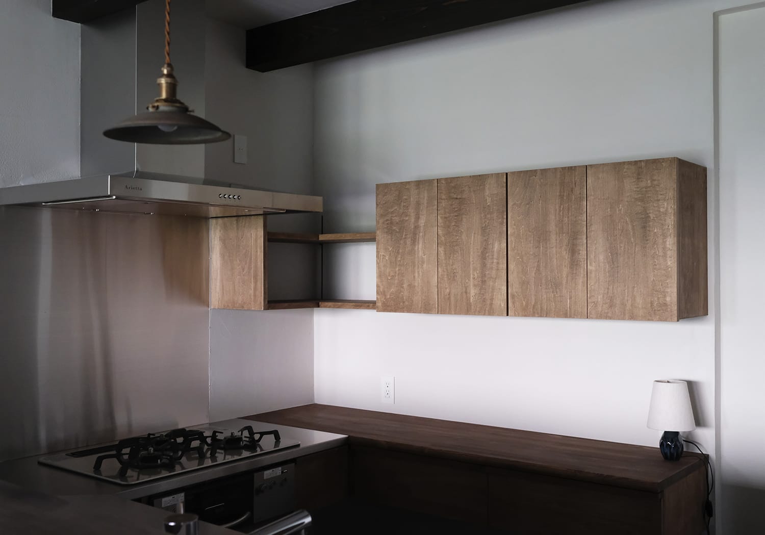 コンパクトでシンプルな木製の作業カウンターと壁付け収納棚のあるキッチン