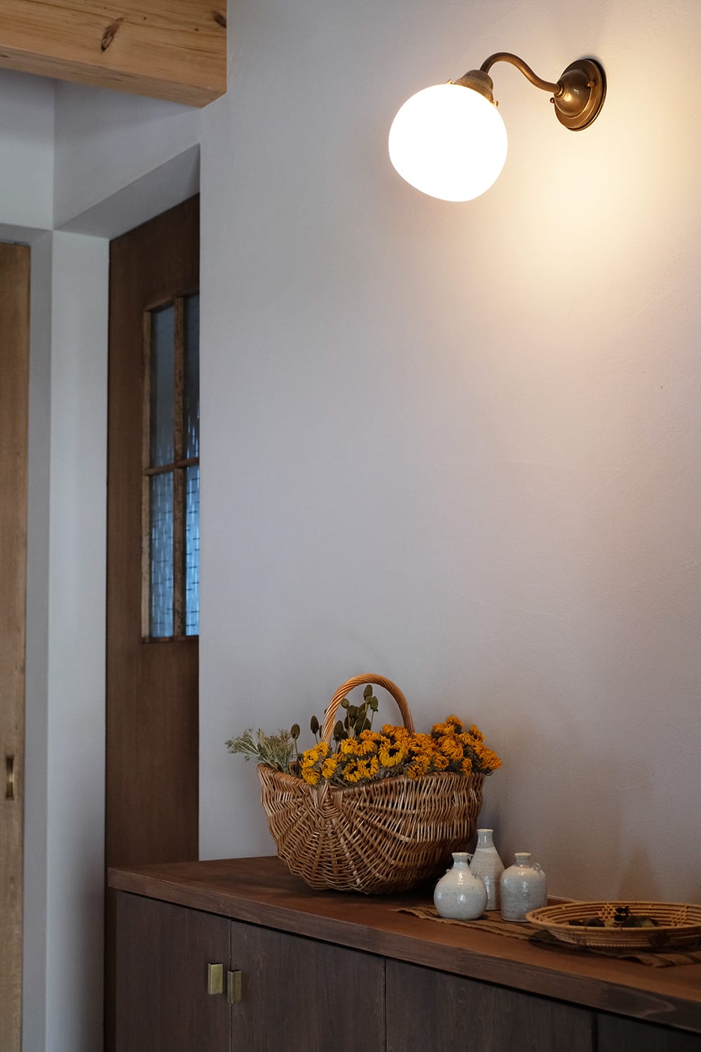 玄関キャビネットの上を飾るドライフラワーと白い陶器と真鍮ランプと引戸のアンティーク型ガラス