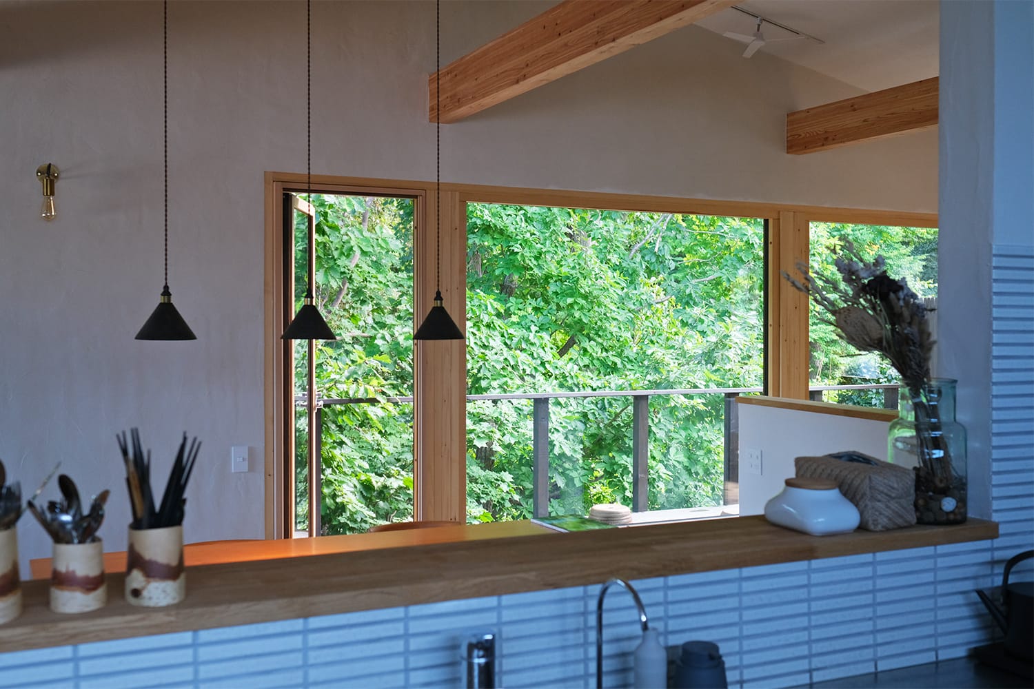 木製窓のガラスが樹々の緑で満たされる 札幌市の森の家のキッチンから