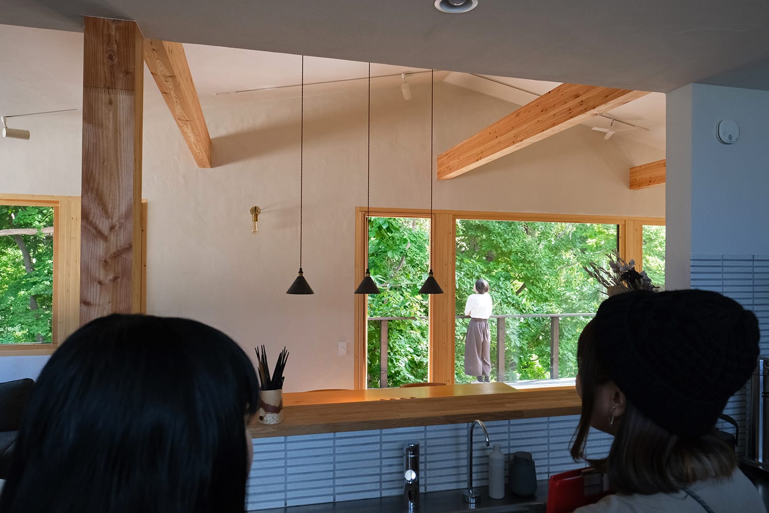 札幌の森の家のキッチンからウッドデッキに佇む建主を見る