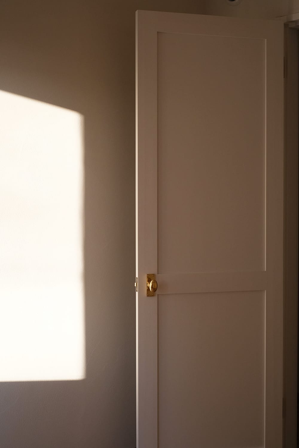 白い左官塗り壁と調和する白塗りの木製ドア真鍮ドアノブ